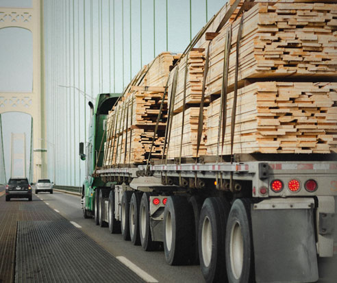 Truck pulling trailer loaded with lumber across suspension bridge.